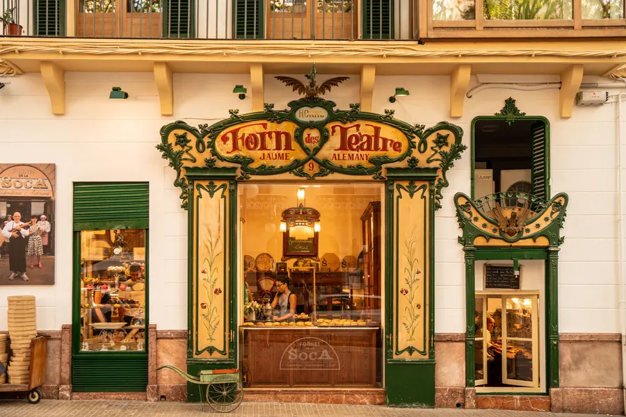 Die Ladenfront der Bäckerei Forn des Teatre an der Plaça de Weyler in Palma, mit grün-goldenem Jugendstilrahmen und Schaufenster.
