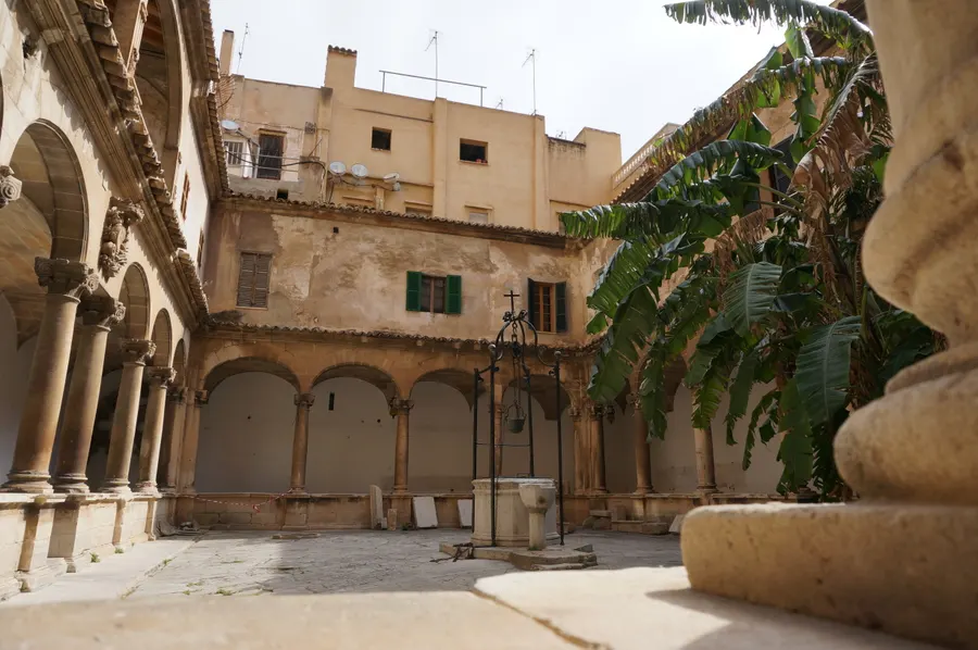 Gotischer Arkadenhof in Palma mit Rundbogengalerie, steinernem Brunnen und einer großen Bananenstaude im Hof.
