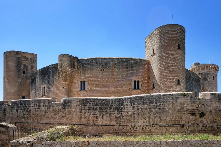 Das Castell de Bellver von außen: eine kreisrunde Burganlage aus hellem Sandstein mit drei angesetzten Rundtürmen, umgeben von einem Wehrgraben.