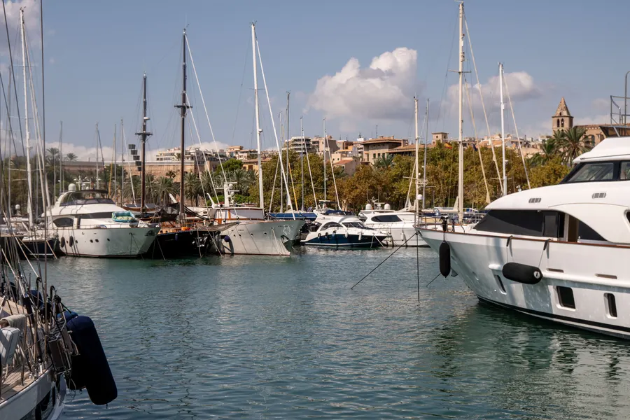 Blick über ein Hafenbecken in Palma auf Yachten, dahinter Häuser der Stadt und ein Kirchturm.
