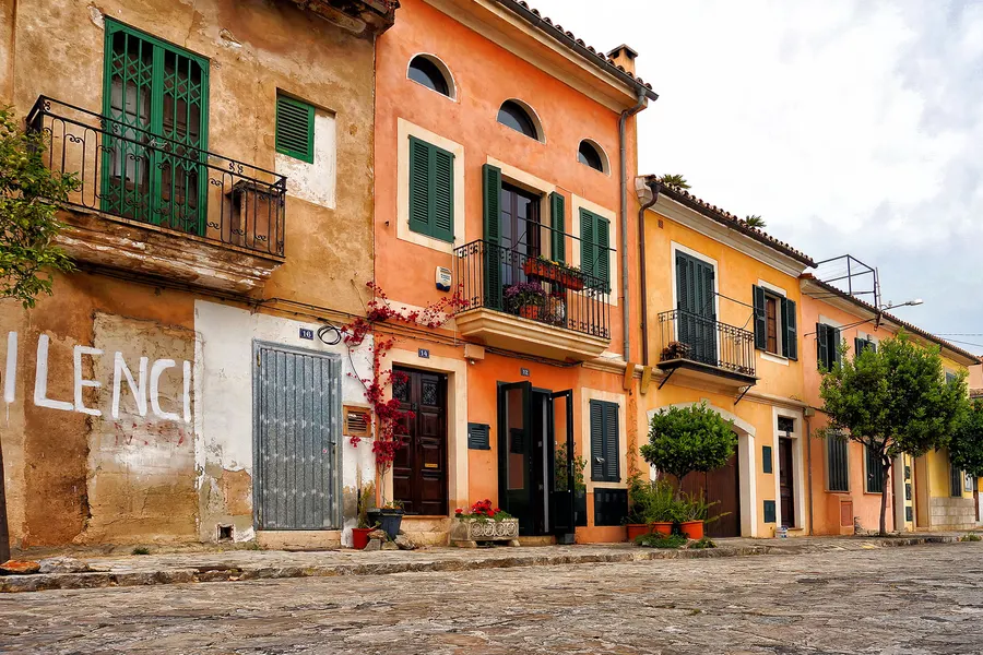 Bunte zweigeschossige Häuserzeile in Santa Catalina in Ocker, Orange und Gelb mit grünen Fensterläden entlang einer ansteigenden Gasse.