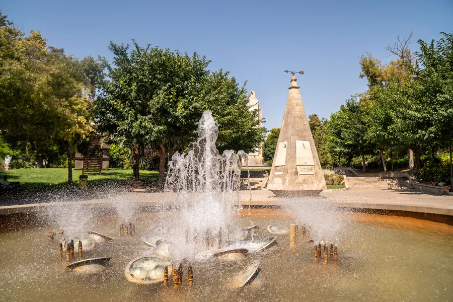 Springbrunnen mit dem Sonnenuhr-Monument im Parc de Sa Feixina in Palma, dahinter Bäume und Grünflächen.