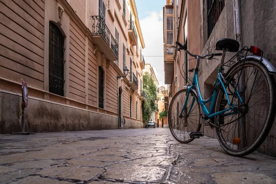 Ein blaues Fahrrad lehnt an einer Hauswand in einer gepflasterten Gasse in Palma.
