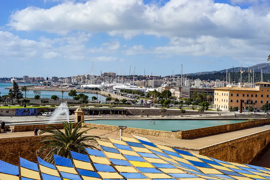 Blick vom Parc de la Mar in Palma über eine blau-gelb gekachelte Fläche und das Wasserbecken auf Hafen und Bucht.
