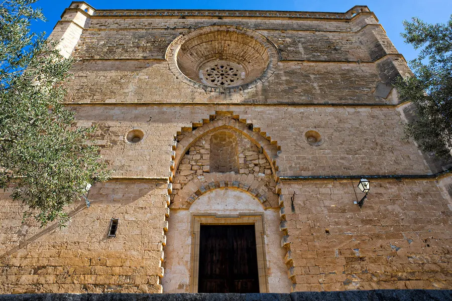 Schlichtes Steinportal mit gestuftem Rundbogen und Rosettenfenster darüber an der Fassade einer Kirche in Petra.

