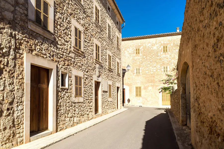 Enge Gasse in Pina zwischen einer hohen Natursteinmauer und einem Wohnhaus, im Hintergrund die Kirchenwand.