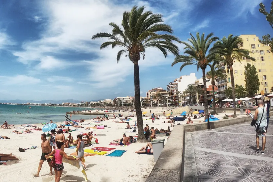Straße in S'Arenal mit Palmen, Souvenirläden unter gelben Markisen und Apartmenthäusern dahinter.
