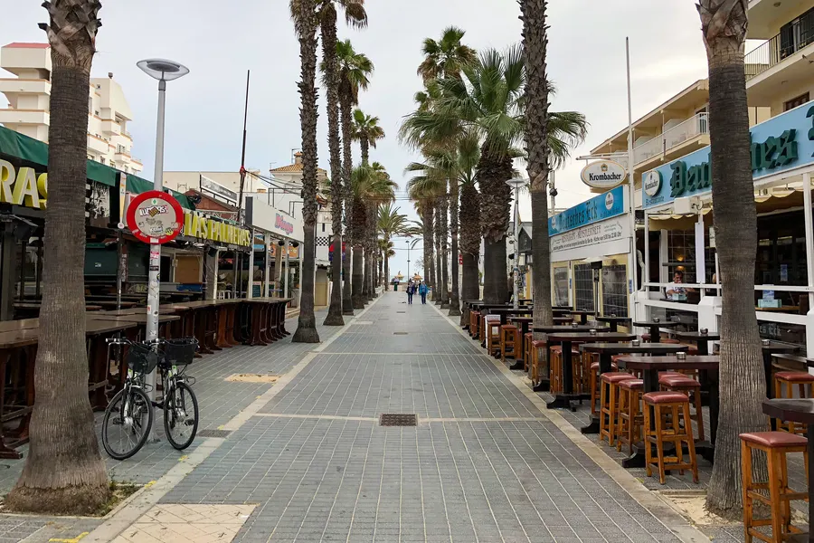 Leere Holzpromenade an der Platja de Palma im Winter, daneben der Sandstrand und das ruhige Meer unter blassem Himmel.
