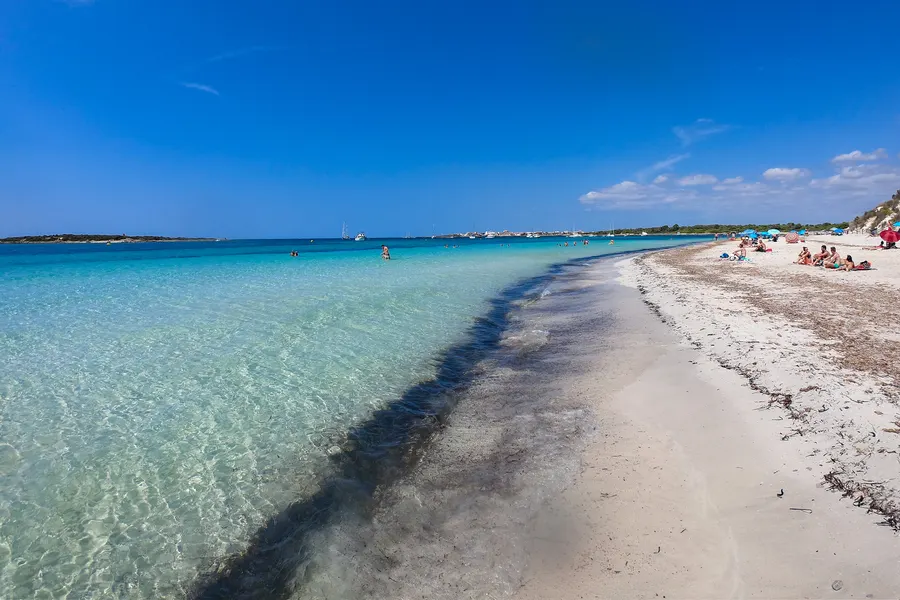 Kristallklares türkisfarbenes Wasser über hellem Sand vor der Platja des Carbó, am Ufer dichte Kiefern.