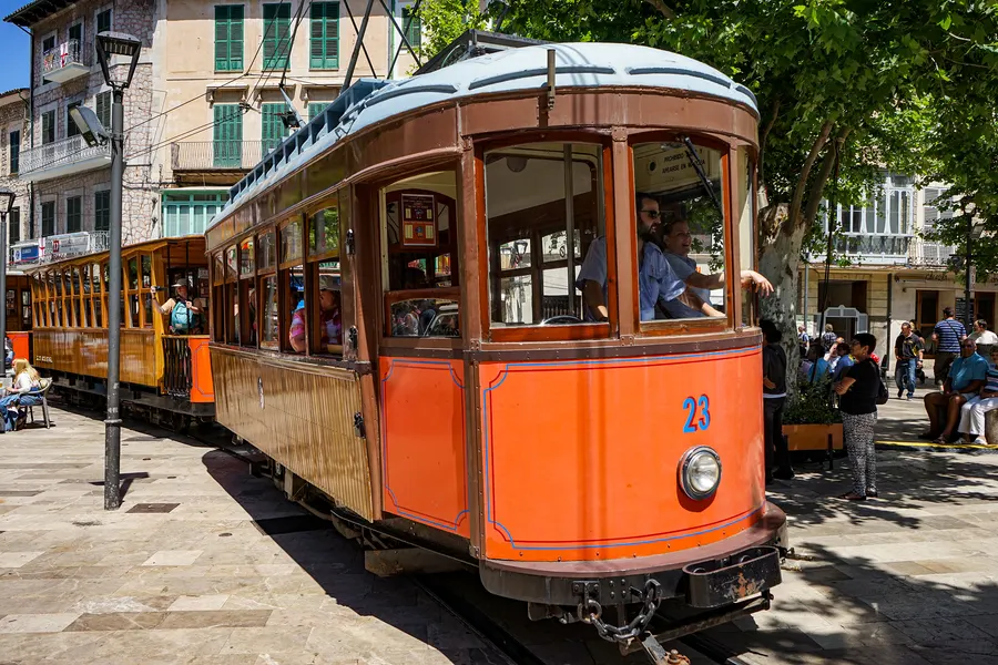 Frontansicht des orangefarbenen Triebwagens Nummer 23 der Straßenbahn Sóller mit Fahrer am Fenster.
