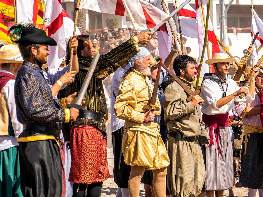 Gruppe als Christen verkleideter Teilnehmer mit Fahnen und Säbeln am Strand von Port de Sóller beim Fest Es Firó.
