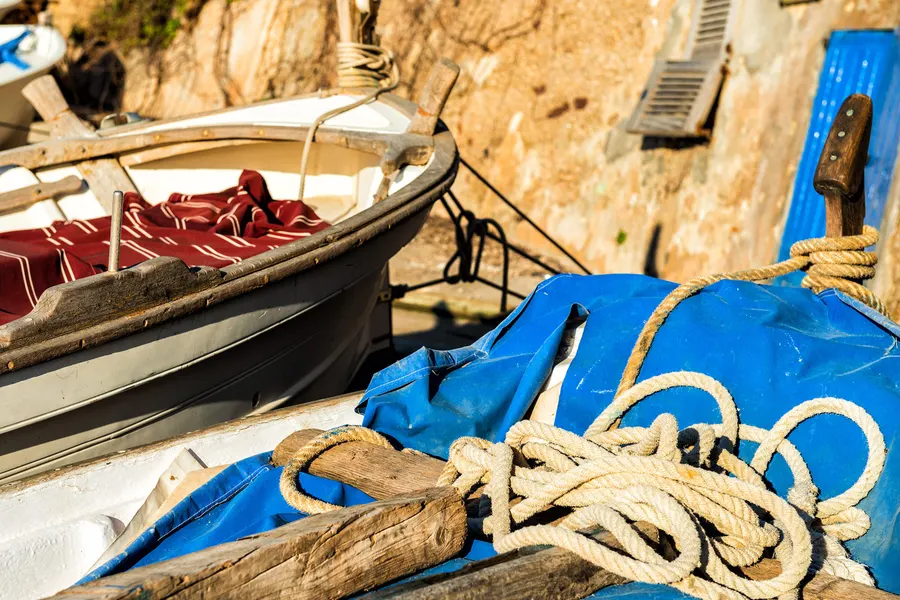 Aufgeschossenes Tauwerk und eine blaue Plane in einem hölzernen Boot in Port de Valldemossa, dahinter die Felswand.