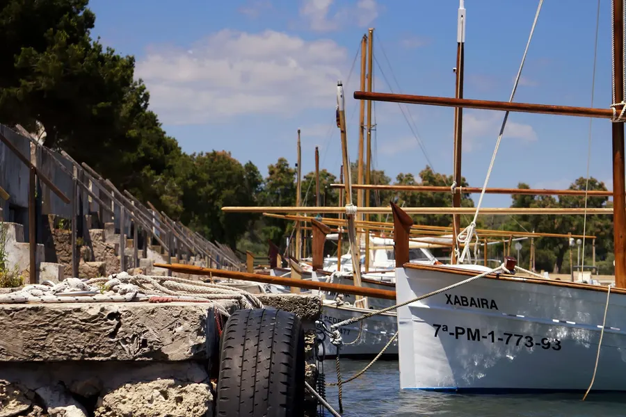 Weißes Fischerboot mit Kennzeichen an der Mole von Portocolom, im Vordergrund eine Gasflasche an Deck.
