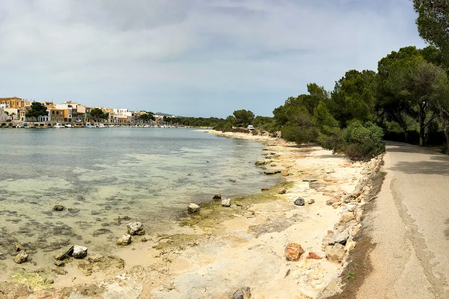 Sandiger Uferweg entlang der flachen Küste in der Bucht von Portocolom, links das seichte Wasser, rechts Kiefern und Macchia.