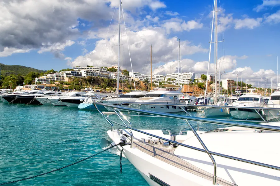 Das Becken von Puerto Portals mit dicht liegenden Motorbooten und Segelyachten, dahinter weiße Terrassenbauten und Kiefern.