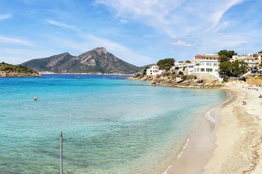 Weite Bucht von Sant Elm mit hellem Sand und türkisem Wasser, am Horizont der lang gestreckte Felsrücken der Insel Dragonera.