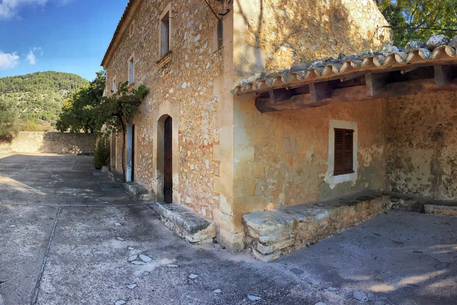 Die schlichte Seitenwand von Sant Miquel im Streiflicht, mit Strebepfeiler, Rundbogentür und Ziegeldach.
