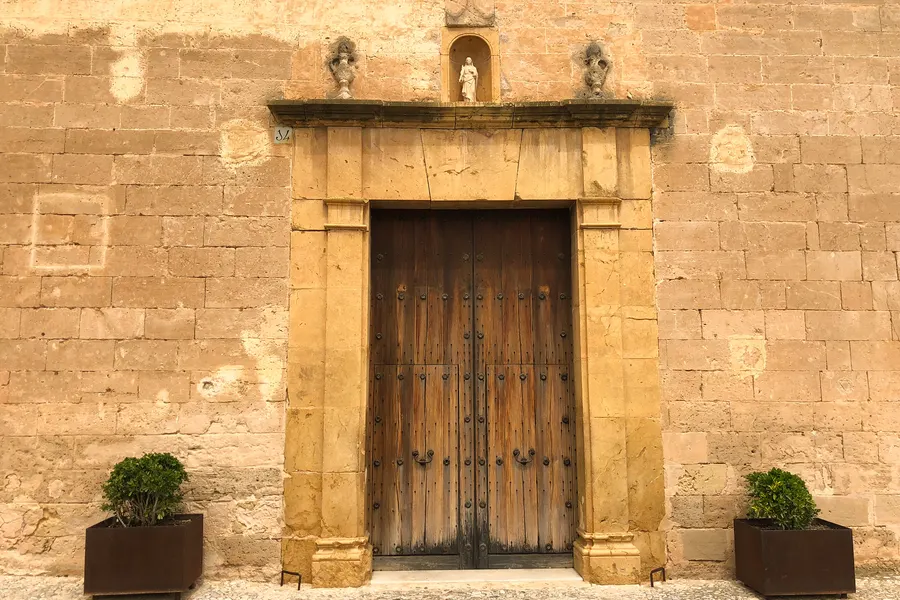 Repräsentatives Portal eines Herrenhauses in Santa Eugènia mit Steingewände, zweiflügeliger Holztür und Kübelpflanzen davor.
