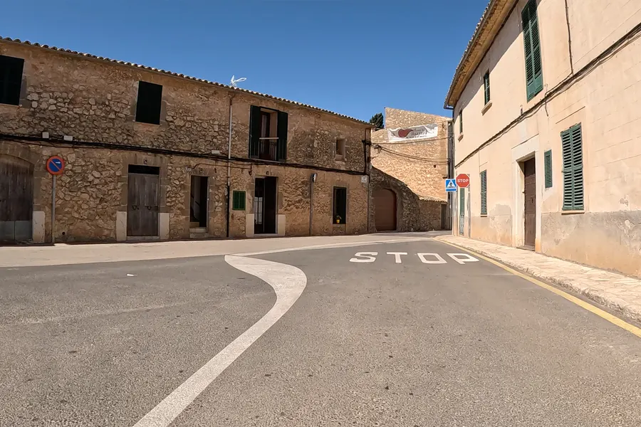 Straßenzug in Santa Maria del Camí mit Natursteinhäusern, großem Torbogen und geschlossenen Fensterläden.