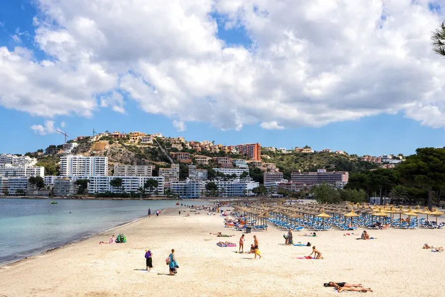Der breite helle Sandstrand von Santa Ponça mit Badegästen und Sonnenschirmreihen, dahinter Hotels und Wohnanlagen am Hang.
