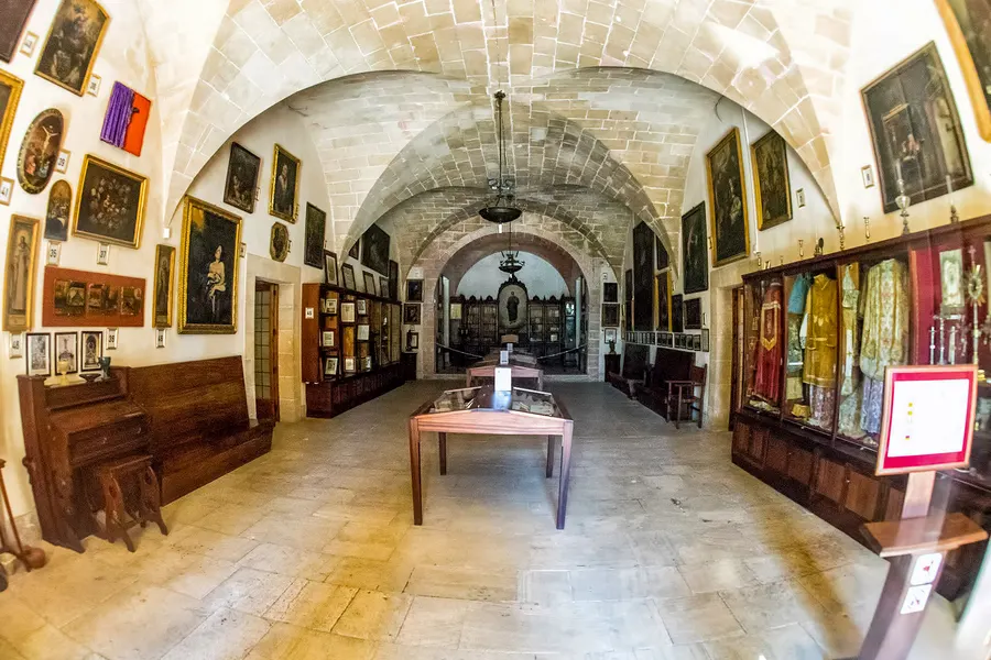 Gewölbter heller Saal des Klosters Cura mit Kreuzrippendecke, an den Wänden gerahmte Bilder und Vitrinen mit Ausstellungsstücken.