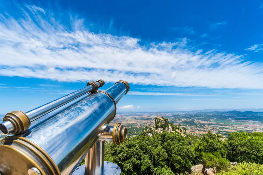 Ein Aussichtsfernrohr aus Metall auf dem Gipfel von Sant Salvador, dahinter die weite Ebene und der Himmel.

