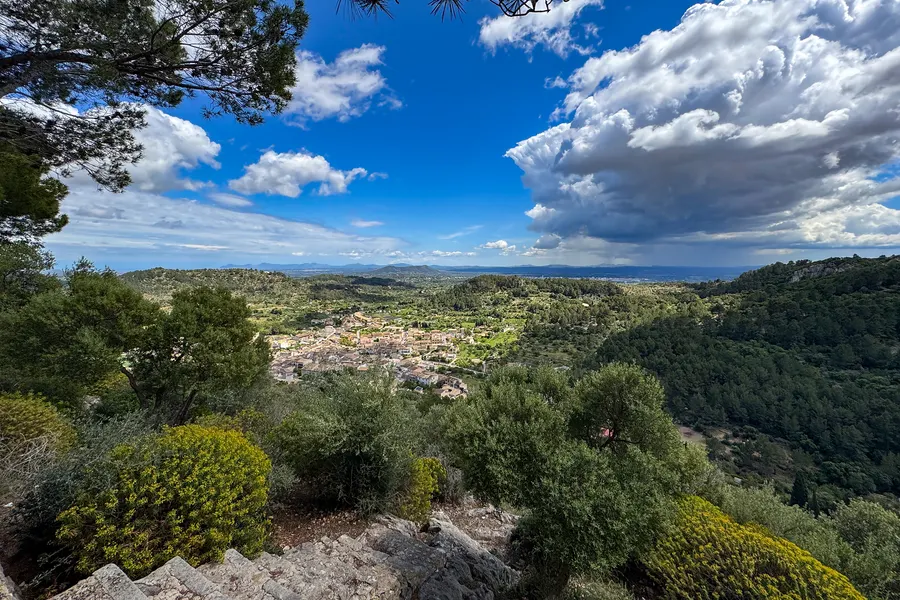 Steinerne Aussichtsterrasse am Santuari de Santa Llúcia mit Stufen und niedrigem Bewuchs, dahinter das Tal und Wolken über der Ebene.