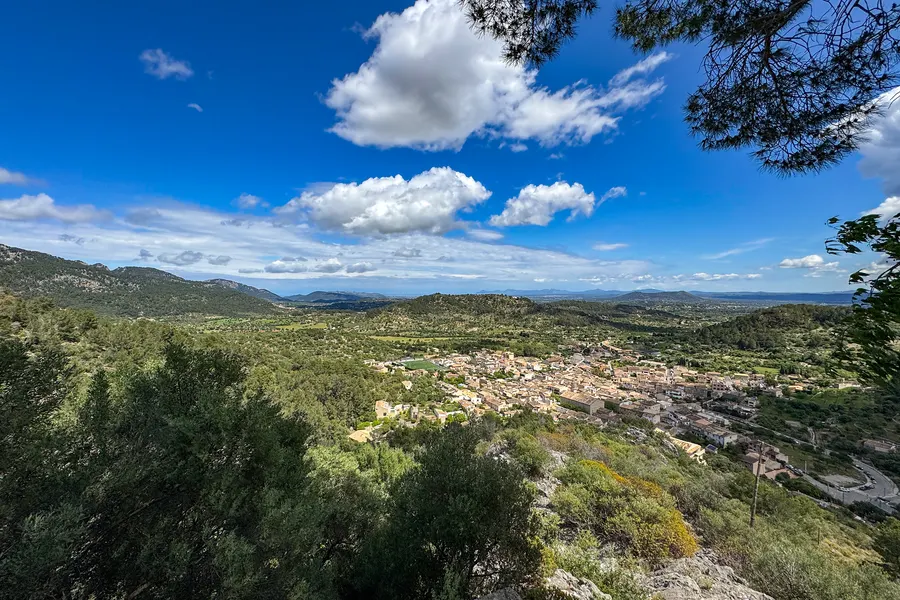 Blick von Santa Llúcia über bewaldete Hänge und Felder nach Osten, unter hohen Quellwolken.