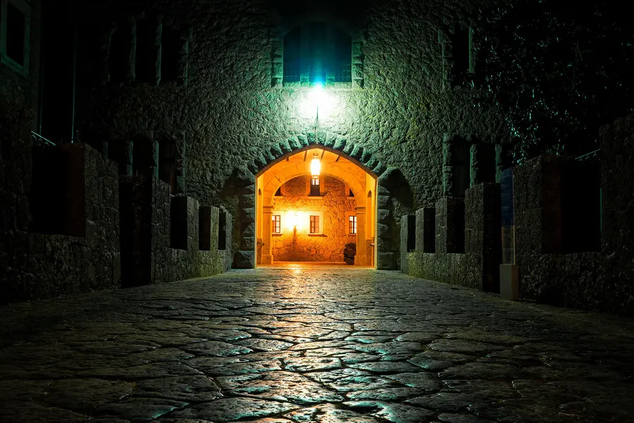 Kreuz auf einer Felsformation über dem Kloster Lluc, umgeben von Bäumen und Sträuchern unter blauem Himmel.
