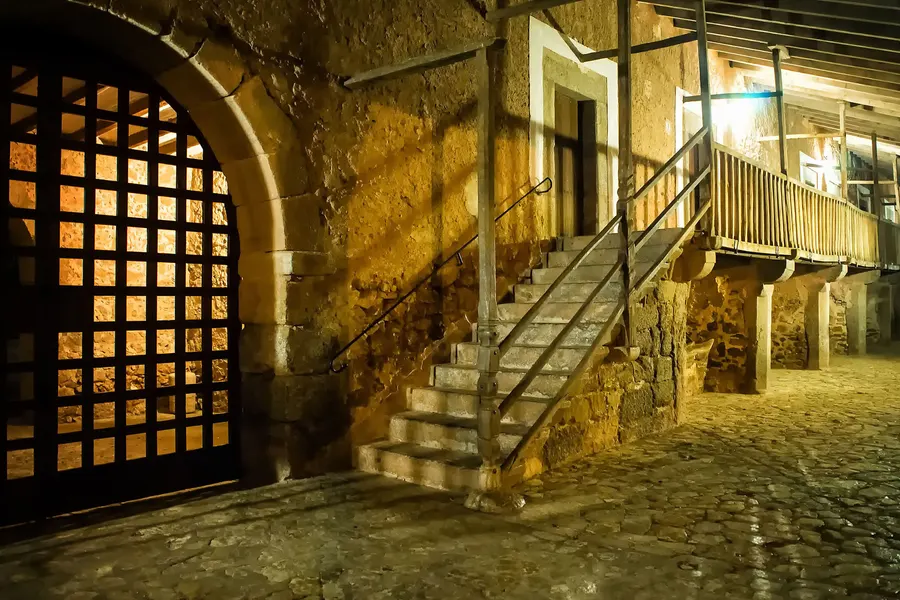 Gewölbter Durchgang im Kloster Lluc mit steinerner Treppe und hölzernem Gitter, dahinter ein heller Innenraum.
