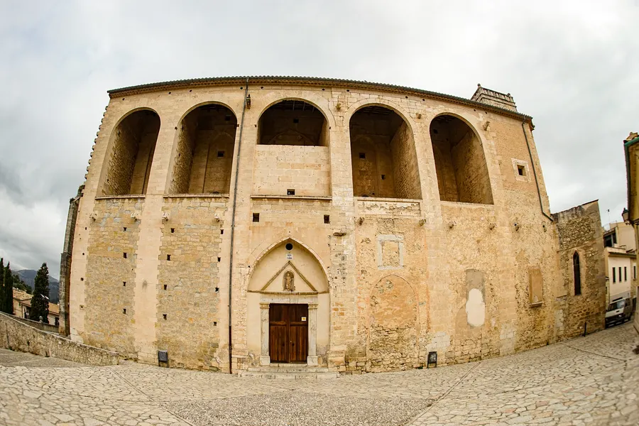 Die mächtige Seitenwand der Kirche von Selva aus hellem Sandstein mit hohen Bogennischen im Obergeschoss und einem gotischen Portal darunter.