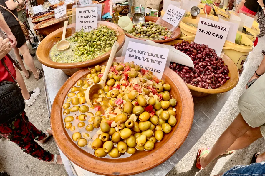 Große Tonschalen mit grünen und dunklen eingelegten Oliven und handgeschriebenen Preisschildern an einem Stand in Sineu.
