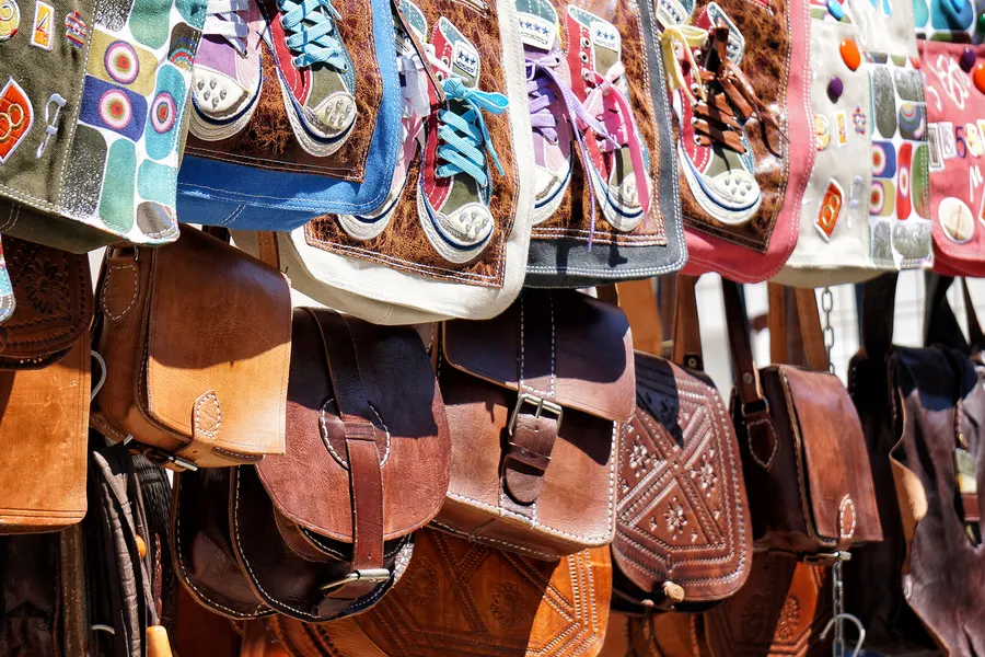 Dicht gehängte Ledertaschen, Rucksäcke und bunte Stoffschuhe an einem Marktstand in Sineu.
