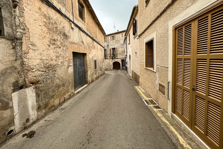 Leicht abfallende Straße in Sineu mit hohen Sandsteinfassaden und breiten hölzernen Hoftoren.
