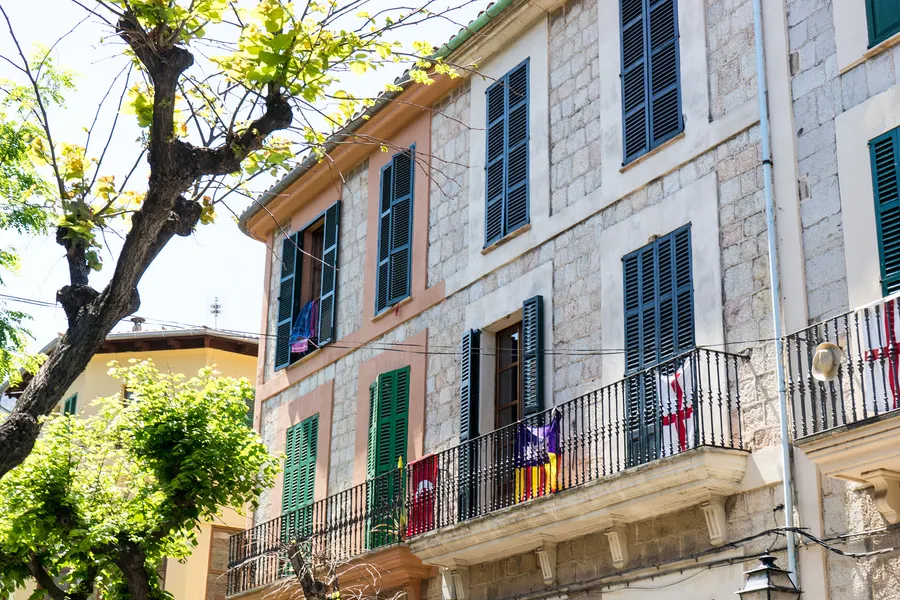 Enge ansteigende Straße in Sóller zwischen hohen Natursteinhäusern mit grünen Läden, am Ende ein Museumsschild.