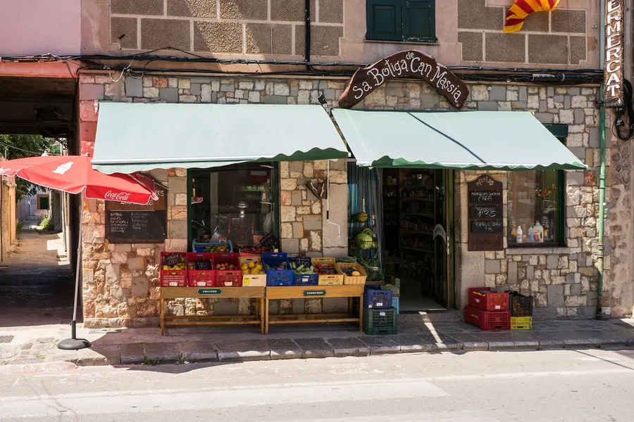 Kleiner Lebensmittelladen in Sóller mit grünen Markisen, Obstkisten davor und einem geschnitzten Ladenschild.
