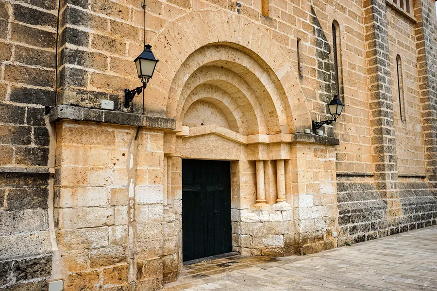 Gestuftes Rundbogenportal der Kirche Sant Miquel mit mehreren Archivolten, schmalen Säulen und einer dunkelgrünen Holztür.