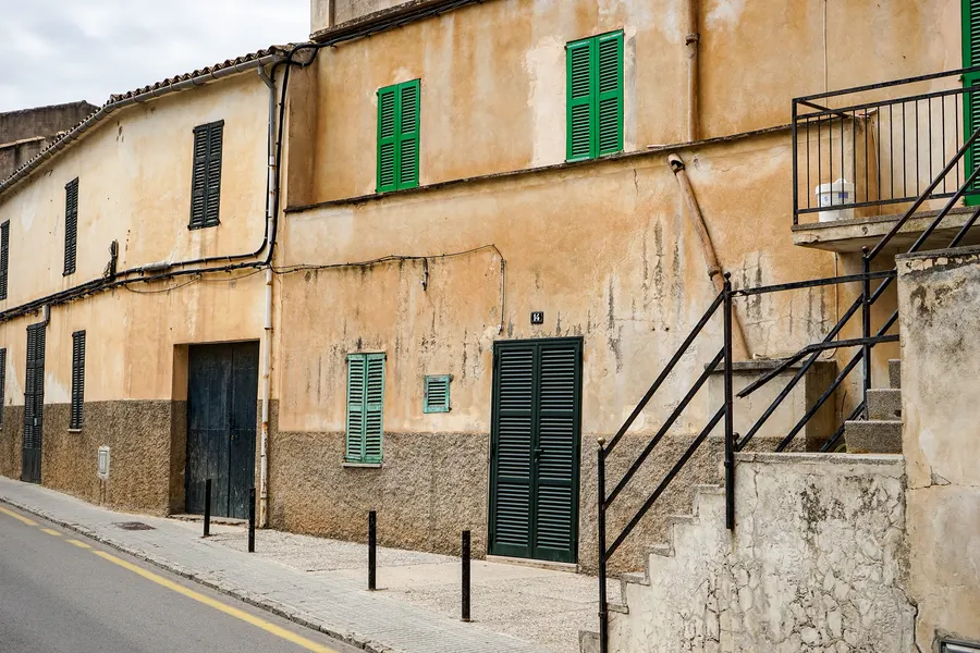 Ockerfarbenes Wohnhaus in Son Carrió mit dunkelgrünen Fensterläden, verwittertem Putz und einer schmalen Außentreppe mit Eisengeländer.
