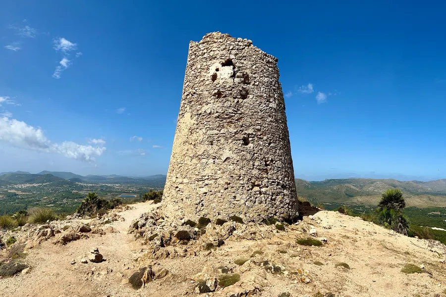 Der Wachturm Torre de Son Jaumell von der Nordseite, mit sichtbaren Maueröffnungen und Bruchsteinmauerwerk, davor Geröll und niedrige Macchia.
