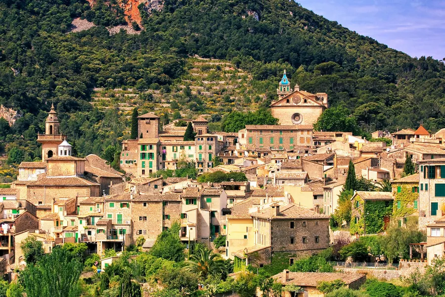 Die Dächer von Valldemossa mit den beiden Türmen von Kartause und Kirche, dahinter der bewaldete Hang des Teix.