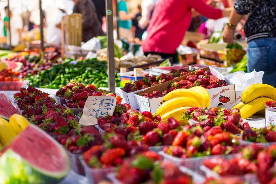 Obststand mit Schalen voller Erdbeeren, dahinter Bananen, Wassermelone und Gemüsekisten.