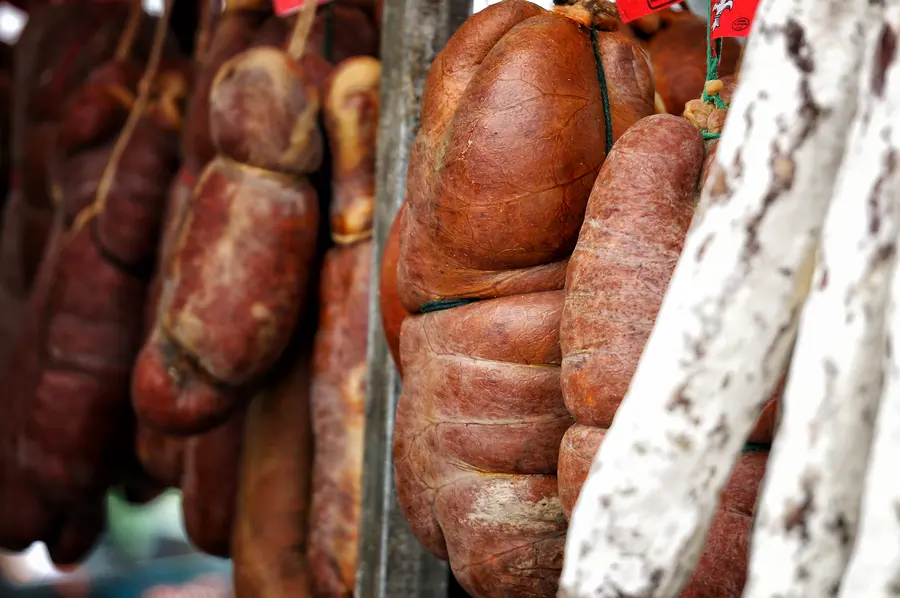 Aufgeschnittene Wurst und Käsestücke nebeneinander auf einer Markttheke, dahinter ganze Laibe und Stangen.